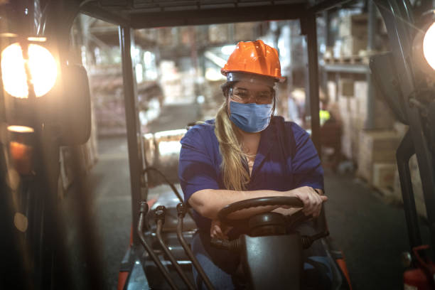 Portrait of female worker driving forklift in warehouse - using face mask Portrait of female worker driving forklift in warehouse - using face mask gender stereotypes stock pictures, royalty-free photos & images