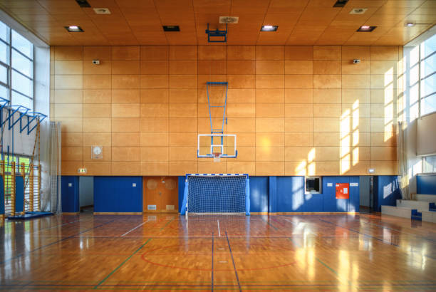 Portrait of Gym and Parquet Basketball Court Wide angle view of empty gym with parquet basketball court and natural light coming through windows. basketball court stock pictures, royalty-free photos & images