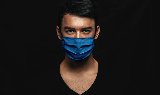검은 벽에 포즈를 취하는 바이러스 전염병 잠금 중 얼굴에 의료 용 파란색 마스크를 착용한 잘생긴 남자의 초상화. 바이러스를 방지하기 위해 일회용 얼굴 마스크백인 남성. 코로나바이러스, 건 - 몰도바 뉴스 사진 이미지