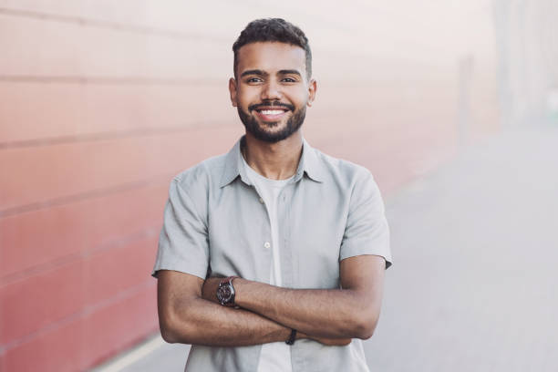 Portrait of handsome smiling young man with folded arms in a city Cheerful young man with crossed hands looking to the camera. one young man only stock pictures, royalty-free photos & images