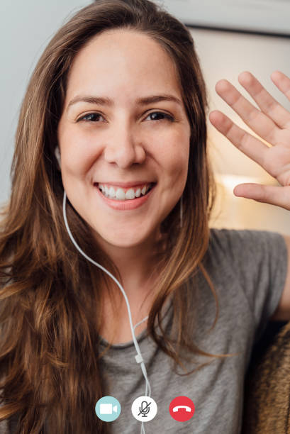 Portrait of happy 30s aged beautiful girl making facetime video calling with smartphone at home. waving on phone screen. Using conferencing meeting online app, social distancing, concept stock photo
