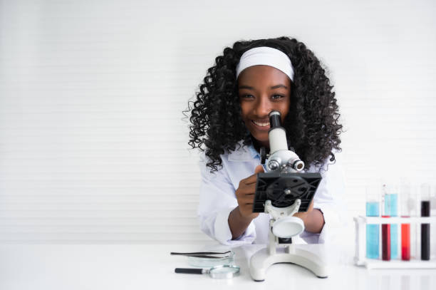 Portrait of happy African American child girl student is learning and test science chemical with colorful liquid by to microscope in laboratory room at school. stock photo