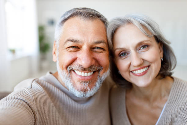 Portrait of happy beautiful senior caucasian couple smiling at camera while making selfie Portrait of happy beautiful senior caucasian family couple smiling at camera, cheerful retired wife and husband making selfie on smartphone while spending time together at home russian mature women pictures stock pictures, royalty-free photos & images