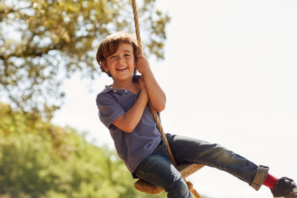 portret van gelukkige jongen spelen op schommel tegen hemel - jongens stockfoto's en -beelden