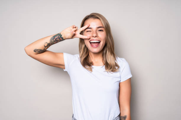 portret van gelukkige vrolijke vrouw die vredesgebaar toont dat over witte achtergrond wordt geïsoleerd - tattoo stockfoto's en -beelden