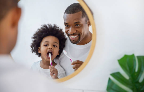 porträt der glücklichen familie schwarz afroamerikanischen vater und sohn kind zähne putzen im badezimmer. morgenroutine mit zahnbürsten, vatertagskonzept - zahnpflege stock-fotos und bilder
