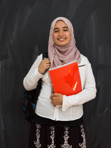 portrait of happy female middle eastern university student against black chalkboard in classroom - arabic student stockfoto's en -beelden