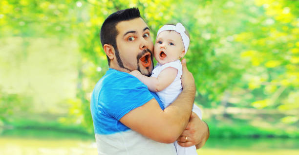 Portrait of happy funny surprised father holding and playing with her baby in summer park stock photo