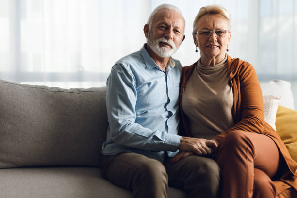 Portrait of happy senior couple sitting on sofa at home stock photo