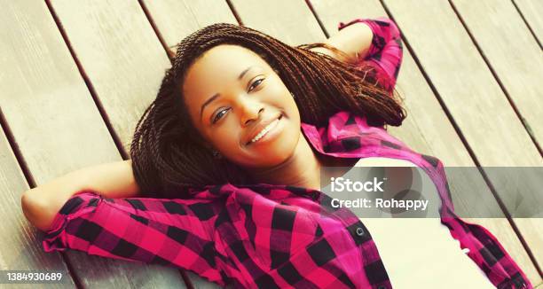 Portrait of happy smiling young african woman relaxing on wooden floor with hands behind head, top view