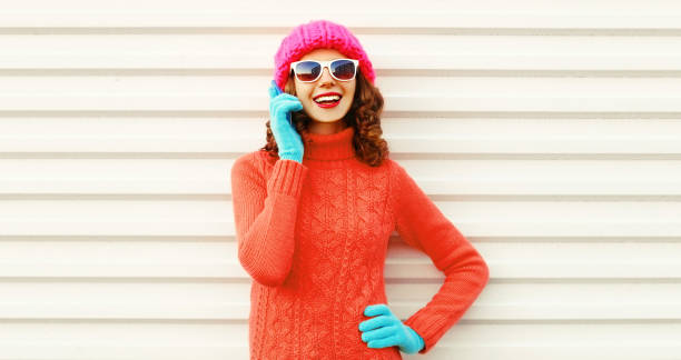 Portrait of happy smiling young woman calling on smartphone wearing a colorful pink knitted hat, sweater on white background stock photo