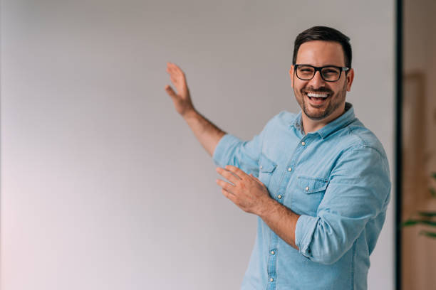 portrait of happy young businessman pointing at white wall - man pointing imagens e fotografias de stock