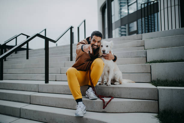 Portrait of happy young man and his dog outdoors in city staircase, looking at camera. stock photo