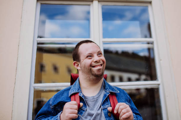 Portrait of happy young man with Down sydrome with backpack in street, smiling. stock photo