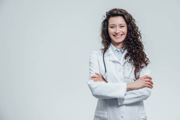 portrait of happy young smiling girl doctor. dressed in a white robe. evenly standing with crossed hands on a gray background. - aluno dentista imagens e fotografias de stock
