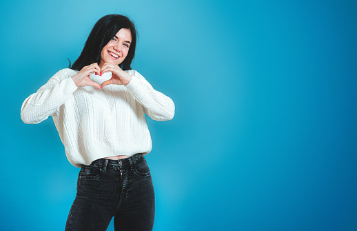 Portrait of lovely young woman showing heart shape with hands. indoor studio shot isolated.