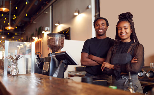 Portrait Of Male And Female Coffee Shop Owners Standing At Sales Desk Portrait Of Male And Female Coffee Shop Owners Standing At Sales Desk Self Employed stock pictures, royalty-free photos & images