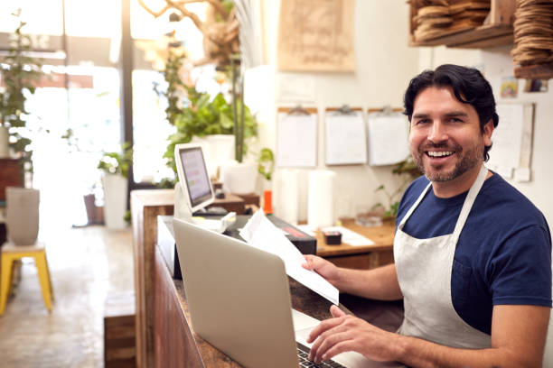 portret van mannelijke verkoopmedewerker die op laptop achter verkoopbureau van de opslag van bloemisten werkt - small business owner stockfoto's en -beelden