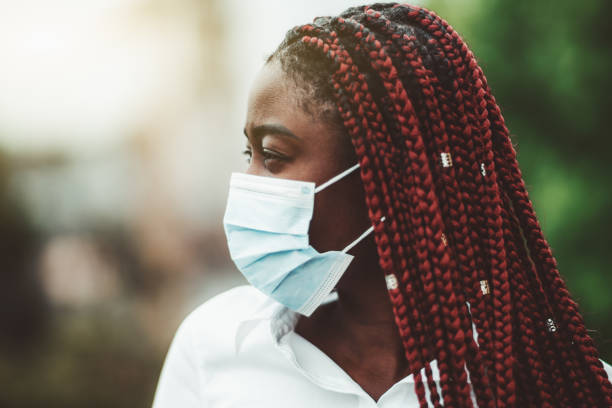 Portrait of masked African woman Close-up portrait of a young African woman with chestnut braids and in a virus protective mask over her face; masked black woman outdoors - protection against influenza and pandemic, selective focus braided hair photos stock pictures, royalty-free photos & images