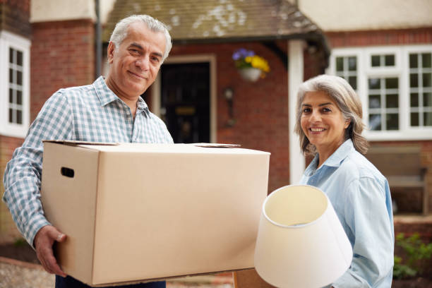 Portrait Of Mature Couple Carrying Boxes On Moving Day In Front Of Dream Home stock photo
