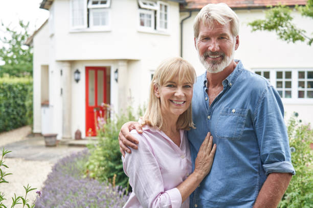 Portrait Of Mature Couple Standing In Garden In Front Of Dream Home In Countryside stock photo