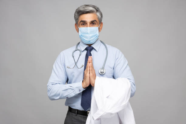 Portrait of mature doctor standing isolated over gray background:- stock photo Adult, male, doctor, India, Indian ethnicity, background namaste greeting stock pictures, royalty-free photos & images