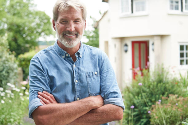 Portrait Of Mature Man Standing In Garden In Front Of Dream Home In Countryside stock photo