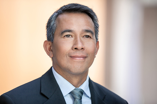 Portrait of mature multiracial Asian businessman in office hallway looking away front view