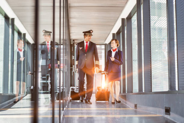 Portrait of mature pilot walking with young attractive stewardess in airport Portrait of mature pilot walking with young attractive stewardess in airport crew stock pictures, royalty-free photos & images