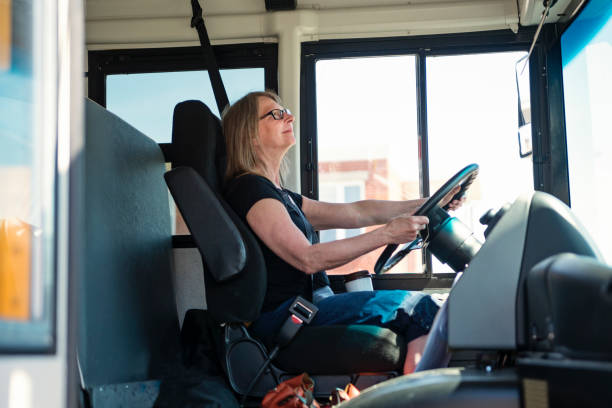 Portrait of mature woman driving a school bus. Portrait of mature woman driving a school bus. She ha her security belt on and two hands on the wheel. Horizontal waist up outdoors shot on a bright sunny day. Copy space. school bus driver stock pictures, royalty-free photos & images
