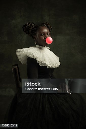 istock Portrait of medieval African young woman in black vintage dress with big white collar posing isolated on dark green background. 1325210343