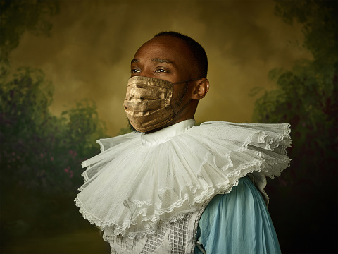Portrait of medieval young man in vintage clothing, golden face mask posing serious, thoughtful on dark background. Royal person protected from covid. Concept of comparison of eras, modern, fashion.