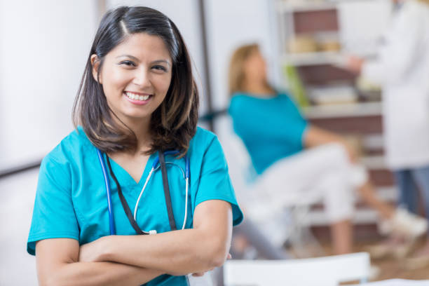 Portrait of mid adult Asian nurse Cheerful mid adult Asian nurse stands confidently in doctor's office or hospital. She has her arms crossed. filipino ethnicity stock pictures, royalty-free photos & images