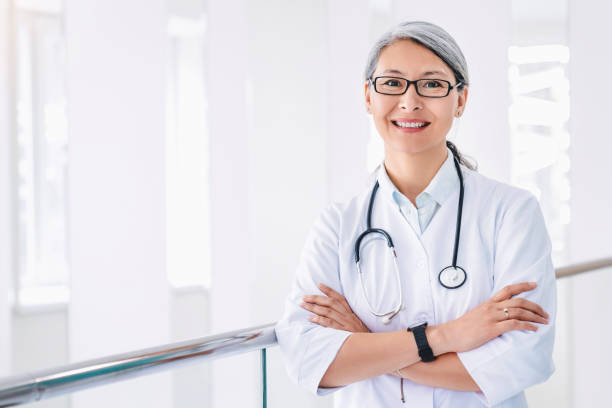 Portrait of middle aged asian female doctor standing in hospital corridor Portrait of middle aged asian female doctor standing in hospital corridor female doctor stock pictures, royalty-free photos & images