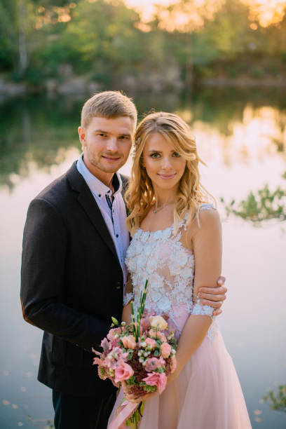 portrait of newlywed couple on the background of a lake at sunset stock photo