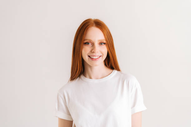 Portrait of positive pretty young woman smiling and looking at camera, standing on white isolated background in studio. stock photo
