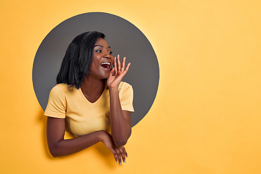Portrait of pretty responsible woman with modern hairdo holding palm near wide open mouth calling someone yelling information announcement loudly isolated on grey circle hole in yellow background.