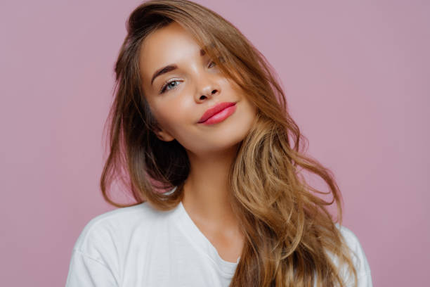 portrait of satisfied relaxed young female model tilts head, has makeup, fair hair, dressed in white clothes, poses against purple background, has well cared complexion. people, beauty, face care - beleza imagens e fotografias de stock