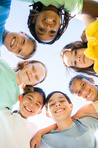 A small group of school aged children huddle closely together with their heads in a circle as they pose for a portrait.  They are each dressed in bright colors and are smiling in this ground view photo.