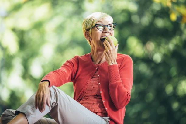 Portrait of senior woman at picnic in park eating green apple. stock photo