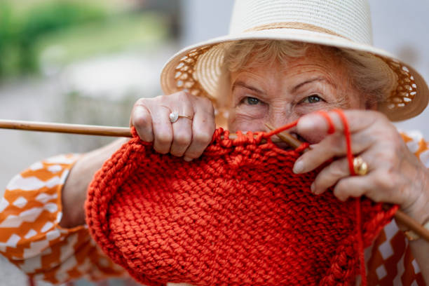 Portrait of senior woman sitting outdoor and knitting red scarf. stock photo