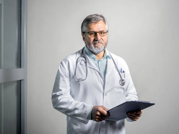 portrait of serious senior doctor with clipboard - doctor wall imagens e fotografias de stock