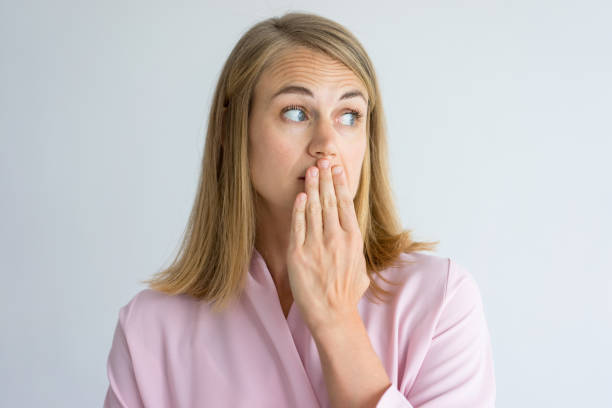 Portrait of shocked young woman covering mouth Portrait of shocked young Caucasian woman wearing pink blouse covering mouth with hand. Fear, bad breath concept bad breath stock pictures, royalty-free photos & images