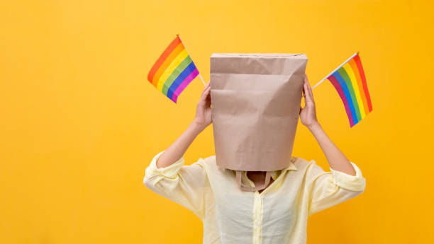 Portrait of shy LGBTQ people covering her face waving rainbow flag for coming out of the closet in pride month to promote marriage equality and differences of homosexual and discrimination concept stock photo