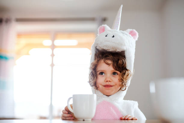 un retrato de niña pequeña en máscara de unicornio sentada en la mesa en casa. - curley cup fotografías e imágenes de stock