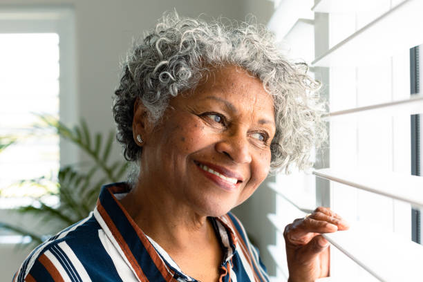 Portrait of smiling african american senior woman looking through window stock photo