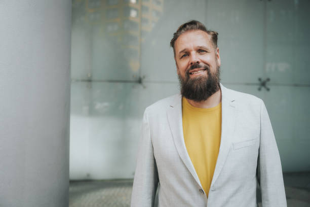 portrait of smiling bearded senior business man in front of glass wall stock photo