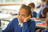 istock Portrait of smiling elementary school girl sitting bored in classroom 534576649