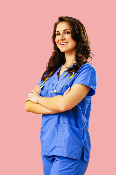 Portrait of smiling female doctor or nurse in blue uniform with arms crossed on pink studio background stock photo