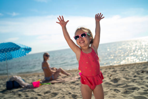 Portrait of smiling girl on the beach Portrait of smiling girl standing on the beach with raised hands. little girls in bathing suits stock pictures, royalty-free photos & images